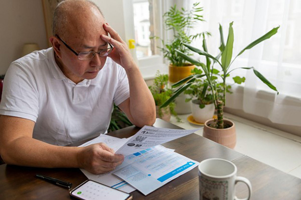 Older Man Reviews Energy Bill While Sitting in Kitchen Older Man Reviews Energy Bill While Sitting in Kitchen